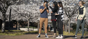 four students work on a film project outdoors on the Vanderbilt campus with white blooming dogwood trees in the background