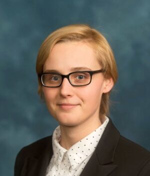 Lucie Kalousova wearing a black blazer, white shirt with black polka dots, and glasses