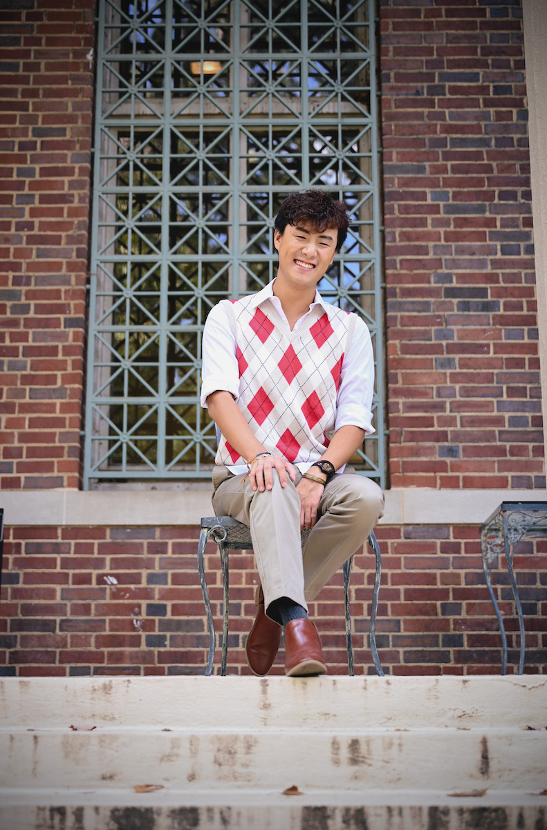 Huang sitting, smiling in front of Cohen