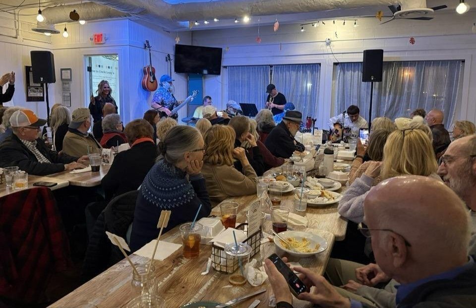 OLLI at Vanderbilt members seated among a large audience at long tables watching live musicians performing inside a casual restaurant.