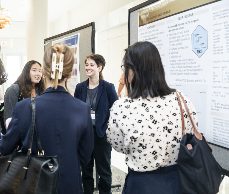 A woman standing in front of her scientific poster discusses it with three others