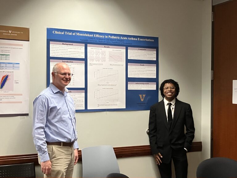 Two men (professor and intern) flank the scientific poster they co-authored