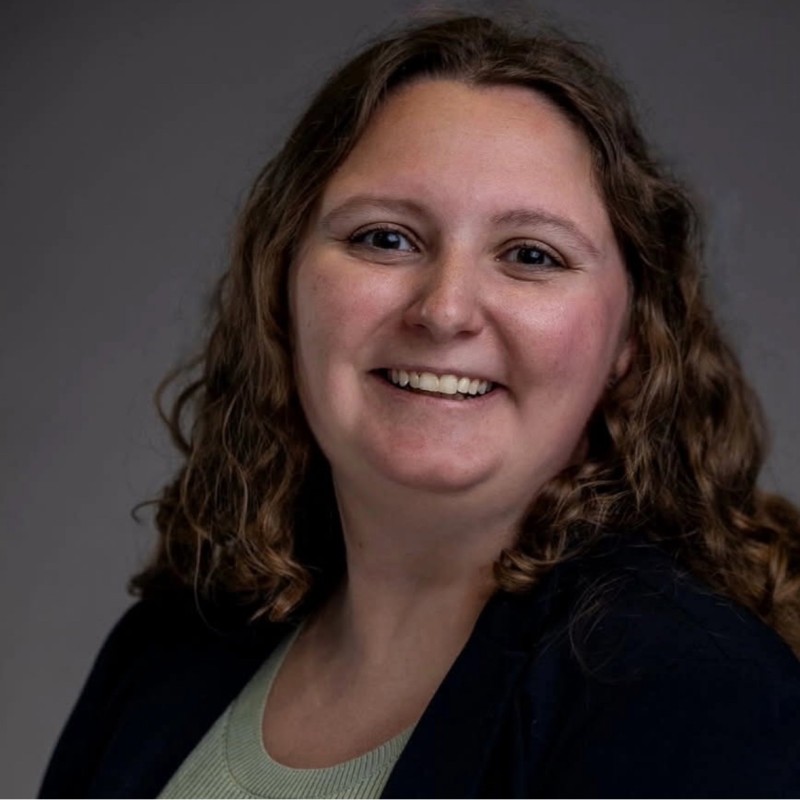 Headshot woman with long curly hair, sage top and dark blazer