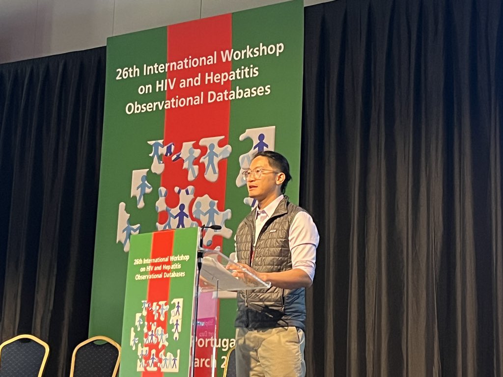 Chinese man wearing quilted vest and button down shirt at lectern in front of colorful conference banner