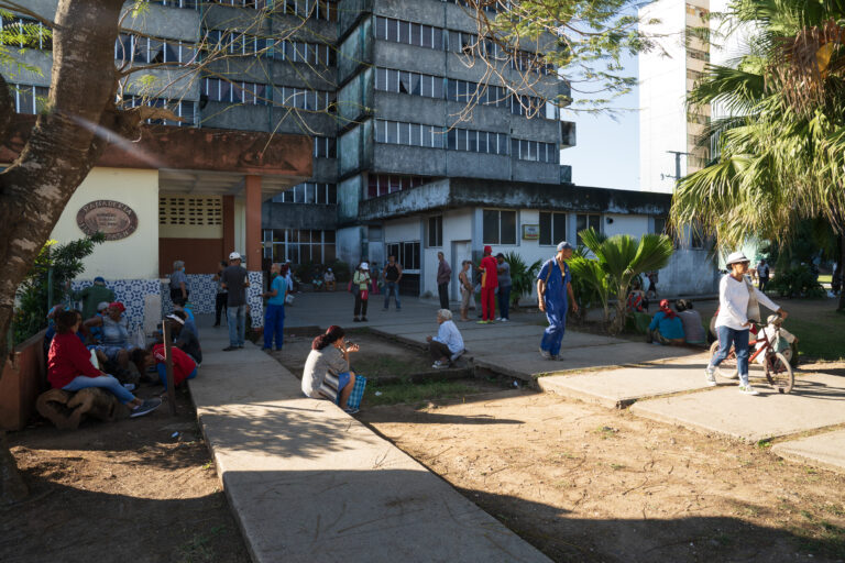 Caption: A crowd waiting in front of a neighborhood bakery (or panadería). The shop is part of a tall apartment block in Matanzas, Cuba. Photograph by Vesna Pavlović.